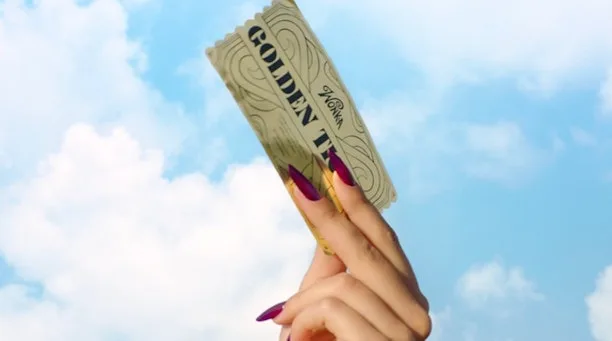 一隻手拎住 Wonka’s The Golden Ticket 金色入場券，後面係藍天同雲