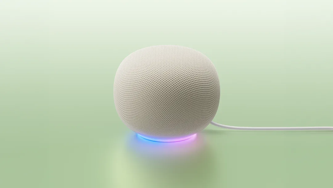 白色 Google Home Speaker 放喺淺綠背景上,底部有彩色燈環發光