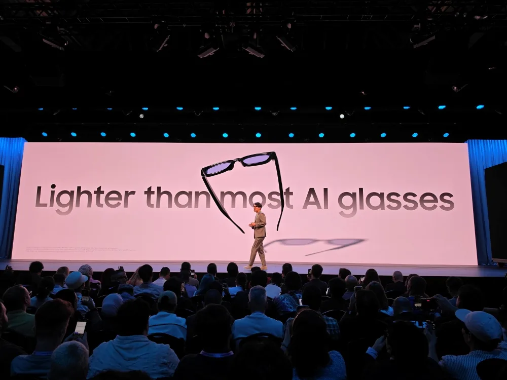 Samsung 喺 Galaxy Unpacked 舞台展示黑色智能眼鏡,背後屏幕強調機身輕巧